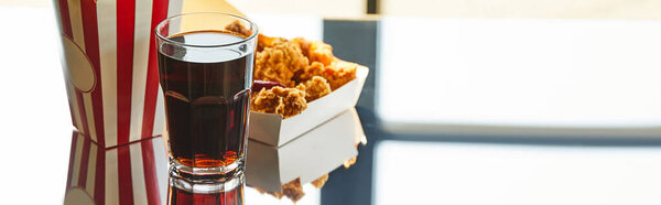 deep fried chicken, striped bucket and soda in glass on glass table in sunlight near window, panoramic orientation