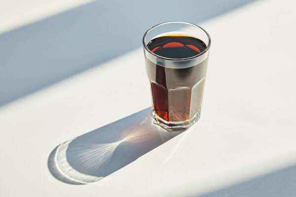 tasty soda in glass on white table in sunlight with shadow