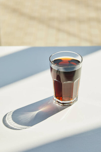 tasty soda in glass on white table in sunlight with shadow near window