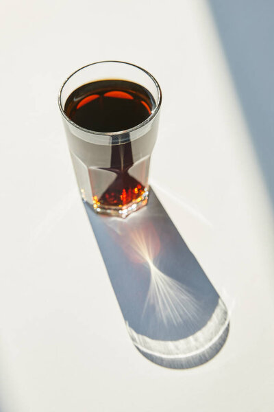 tasty soda in glass on white table in sunlight with shadow