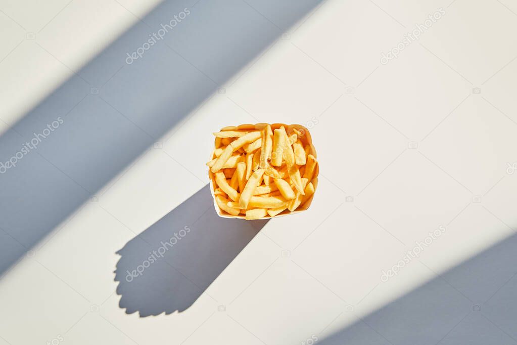top view of tasty french fries in bucket on white table in sunlight