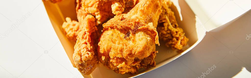 close up view of tasty deep fried chicken with chili pepper on white table in sunlight, panoramic crop