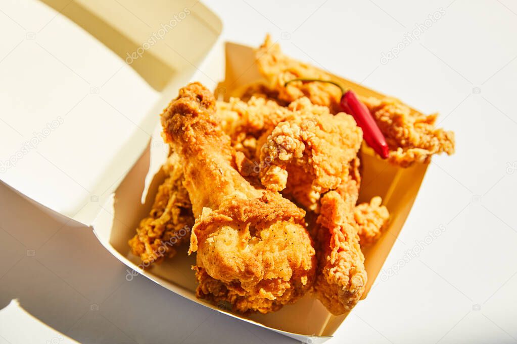 close up view of tasty and spicy deep fried chicken with chili pepper on white table in sunlight