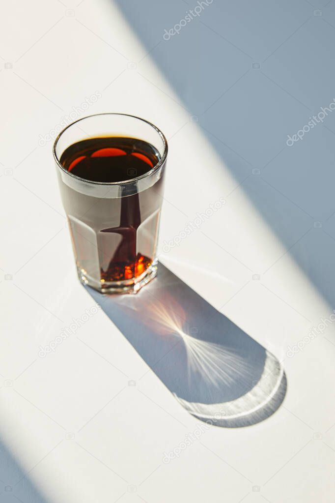 tasty soda in glass on white table in sunlight with shadow