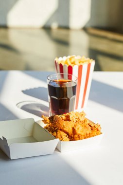selective focus of tasty deep fried chicken, french fries and soda in glass on white table in sunlight clipart