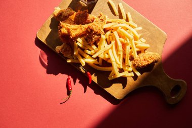 Baharatlı, yağda kızartılmış tavuk ve patates kızartması güneş ışığında ahşap kesme tahtasında servis edilir.