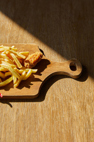 top view of deep fried chicken, french fries on board on wooden table in sunlight