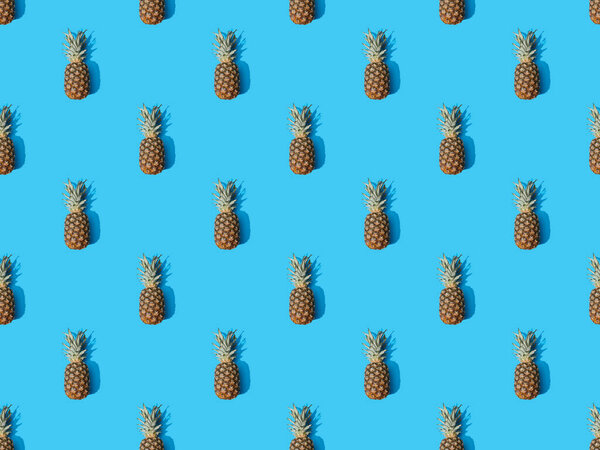 top view of whole ripe pineapples on blue colorful background, seamless pattern