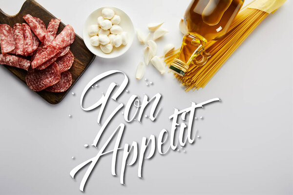 Top view of bottle of olive oil, meat platter, garlic, pasta and bowl with mozzarella on white, bon appetit illustration