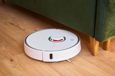 Robotik süpürge, yeşil kanepenin yanında yerleri yıkıyor.