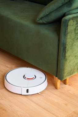 modern otomatik elektrikli süpürge oturma odasındaki yeşil kanepenin yanında yerleri yıkıyor. 