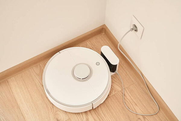 top view of modern robotic vacuum cleaner near power socket on wall 