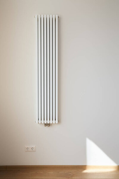 white and modern heating radiator near wall with power sockets 