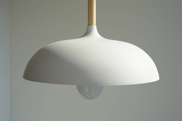close up of white and modern lamp with light bulb near wall