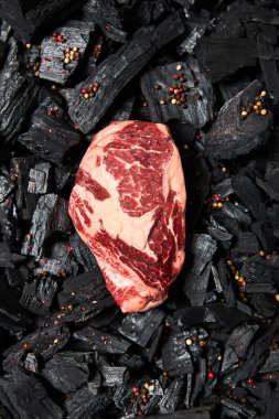 top view of fresh raw steak on black coals with peppercorns clipart