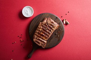 top view of tasty grilled steak served on wooden board on red background with salt and pepper clipart