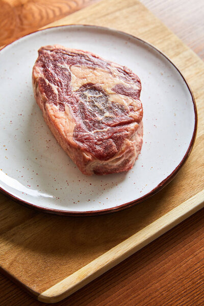 свежий стейк на тарелке на раскройке доски на деревянном столе
