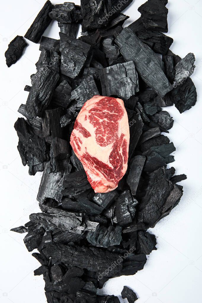 top view of fresh raw steak on black coals on white background