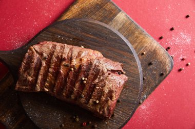top view of tasty grilled steak served on wooden board on red background with pepper and salt clipart