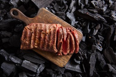 top view of cut fresh grilled tasty steak with rare roasting on wooden cutting board on black coals clipart