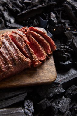 cut fresh grilled tasty steak with rare roasting on wooden cutting board on black coals clipart