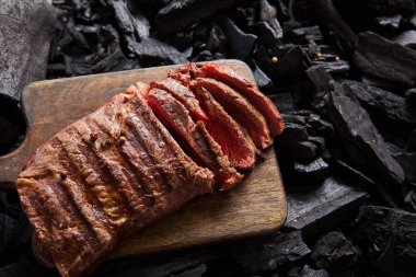 top view of cut fresh grilled tasty steak with rare roasting on wooden cutting board on black coals clipart