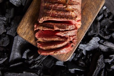 top view of cut fresh grilled tasty steak with rare roasting on wooden cutting board on black coals clipart