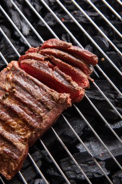 cut fresh grilled tasty steak with rare roasting on grate above black coals clipart