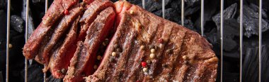 top view of cut fresh grilled tasty steak with rare roasting and condiments on grate above black coals, panoramic shot clipart
