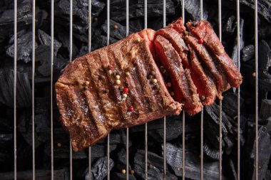 top view of cut fresh grilled tasty steak with rare roasting and condiments on grate above black coals clipart