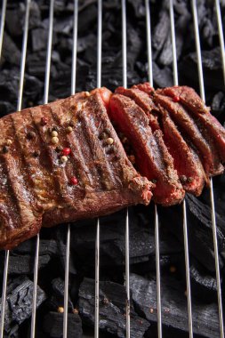 cut fresh grilled tasty steak with rare roasting and condiments on grate above black coals clipart