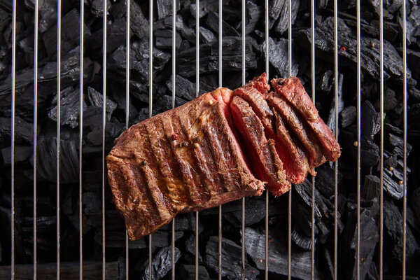 top view of cut fresh grilled tasty steak with rare roasting on grate above black coals