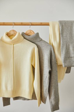 bej ve gri örgü yumuşak süveterler ve pantolonlar beyaz askılarda asılı.