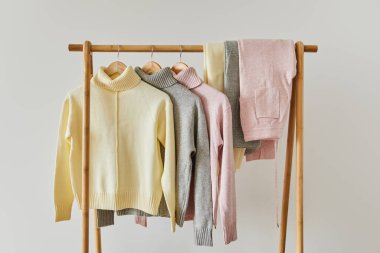 pembe, bej ve gri örülmüş yumuşak süveterler ve pantolonlar ahşap askılarda asılı beyaz üzerinde izole