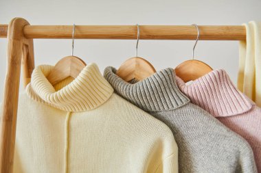 Pembe, bej ve gri örülmüş yumuşak süveterler ahşap askıda asılı, beyaz üzerine izole edilmiş.