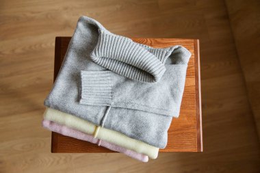 Üstten pembe, bej ve gri örülmüş yumuşak kazaklar odasındaki ahşap masada.