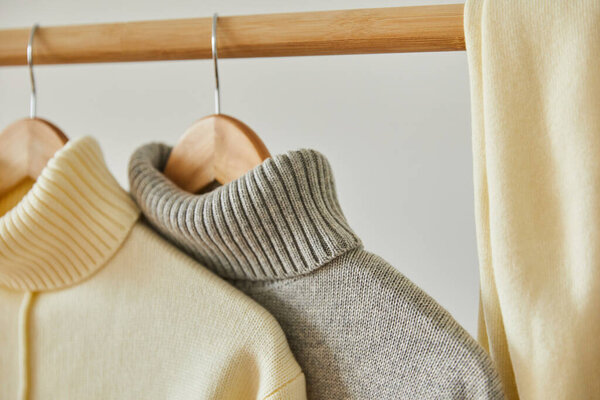 close up view of beige and grey knitted soft sweaters hanging on wooden hangers isolated on white