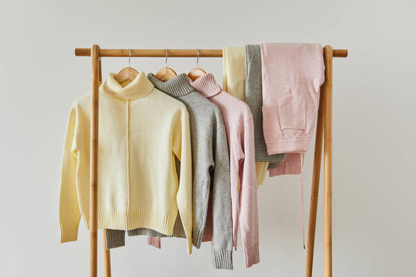 pink, beige and grey knitted soft sweaters and pants hanging on wooden rack isolated on white