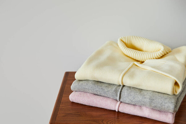 pink, beige and grey knitted soft sweaters on wooden table isolated on white