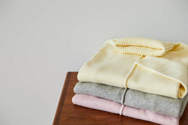 pink, beige and grey knitted soft sweaters on wooden table isolated on white