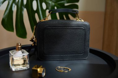 leather handbag near golden earrings, perfume on black table near tropical leaf clipart