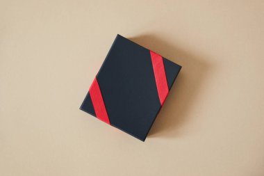 Bej arka planda kırmızı kurdeleli siyah hediye kutusunun üst görünümü 