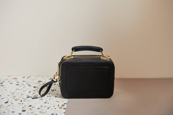leather black handbag with golden zippers on marble surface on beige background