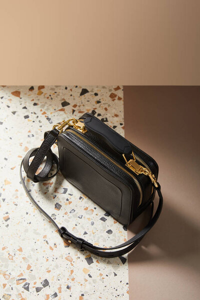 leather black handbag with golden zippers on marble surface on beige background