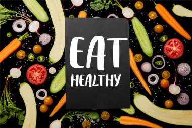 top view of black card with eat healthy illustration on vegetable pattern isolated on black clipart