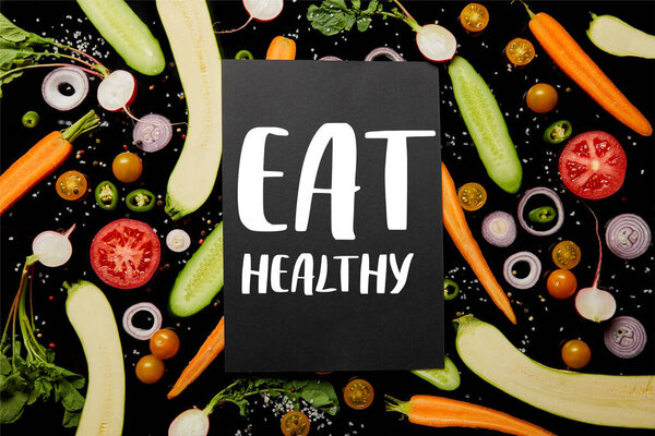 top view of black card with eat healthy illustration on vegetable pattern isolated on black