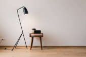 kovová podlahová lampa a dřevěný konferenční stolek s rostlinou a hodinami s prázdnou obrazovkou