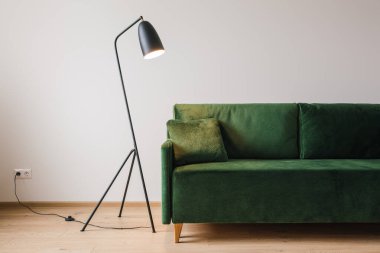 Modern metal lambanın yanında yastıklı yeşil kanepe