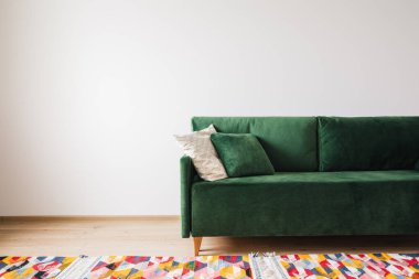 Geniş odada yastıklı, renkli halılı modern yeşil kanepe.