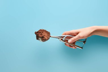 cropped view of woman holding scoop with chocolate ice cream on blue background clipart
